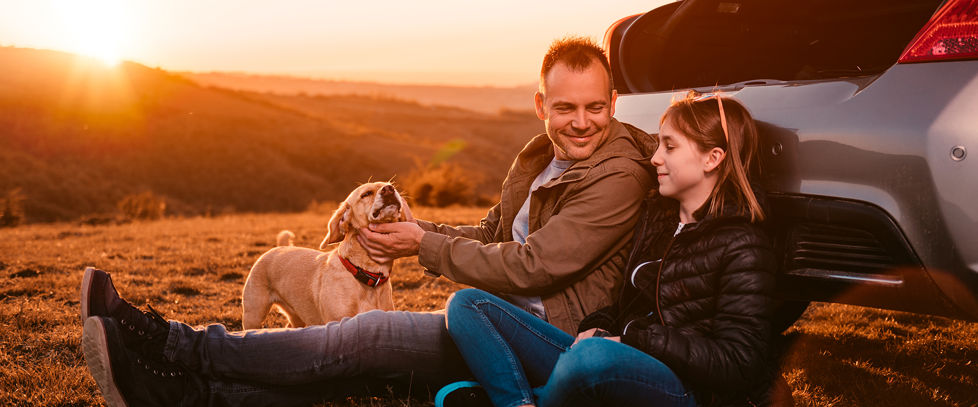 Een vader en dochter zittens amen voor een auto en kijken elkaar aan.